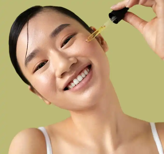 Close-up smiling woman applying golden serum with a dropper for a radiant, hydrated glow